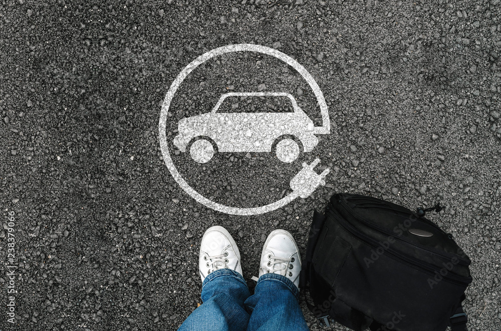a man with a shoes is standing next to electric car sign on road asphalt - obrazy, fototapety, plakaty 