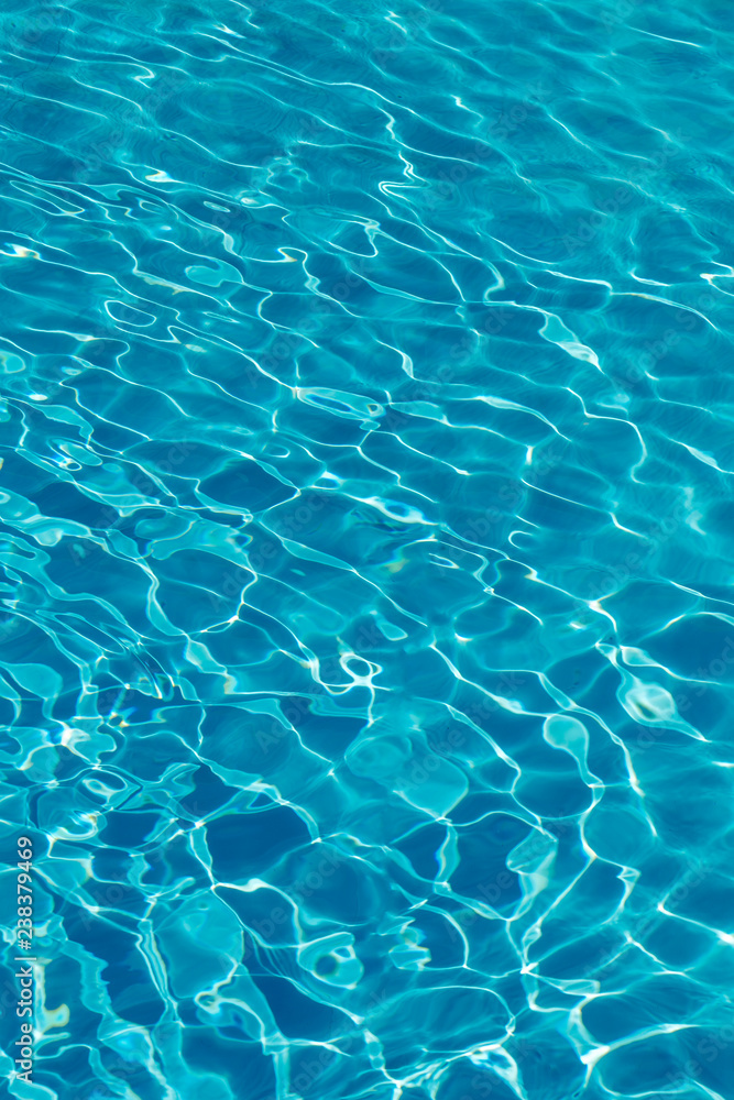 Blue water in swimming pool background. Ripple Water in swimming pool with sun reflection. Blue swimming pool rippled water detail. vertical photo