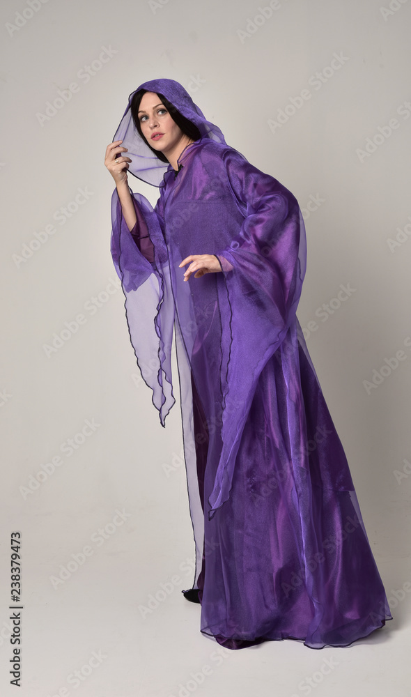 full length portrait of beautiful girl with long black hair, wearing purple fantasy medieval gown and cloak. standing pose on grey studio background. full length portrait of beautiful girl with long black hair, wearing purple fantasy medieval gown and cloak. standing pose on grey studio background.