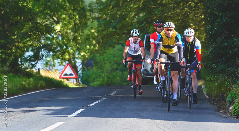 A group of cyclists on a bike race on a sunny day along country roads in the UK.