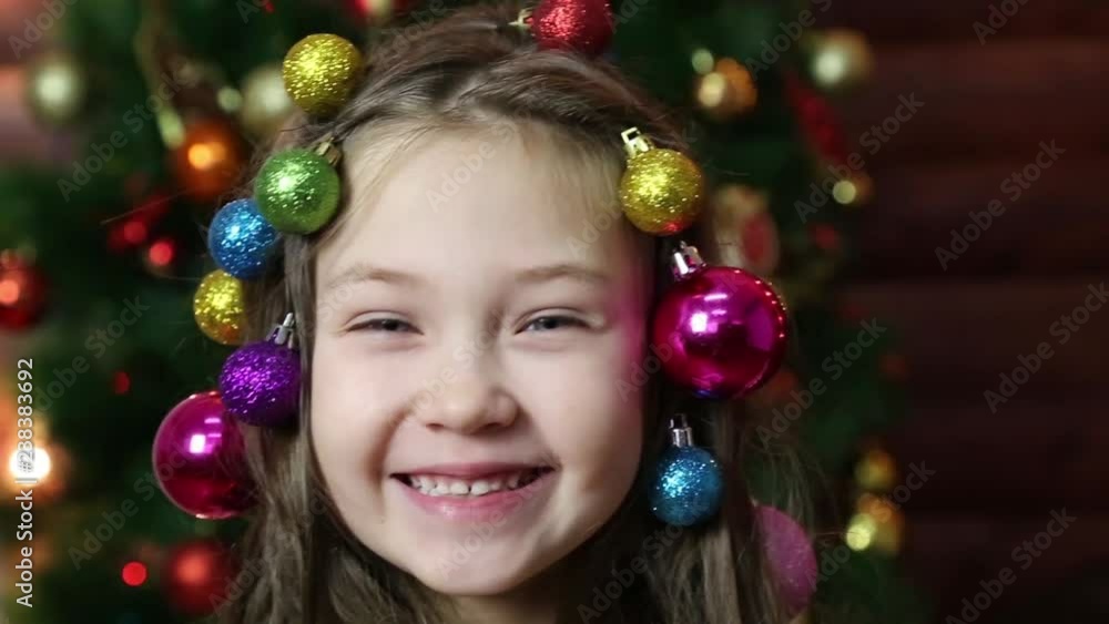Girl with Christmas decorations in her hair. Little beautiful girl braided Christmas tree decorations in her hair. Girl with Christmas decorations in her hair. Little beautiful girl braided Christmas tree decorations in her hair.