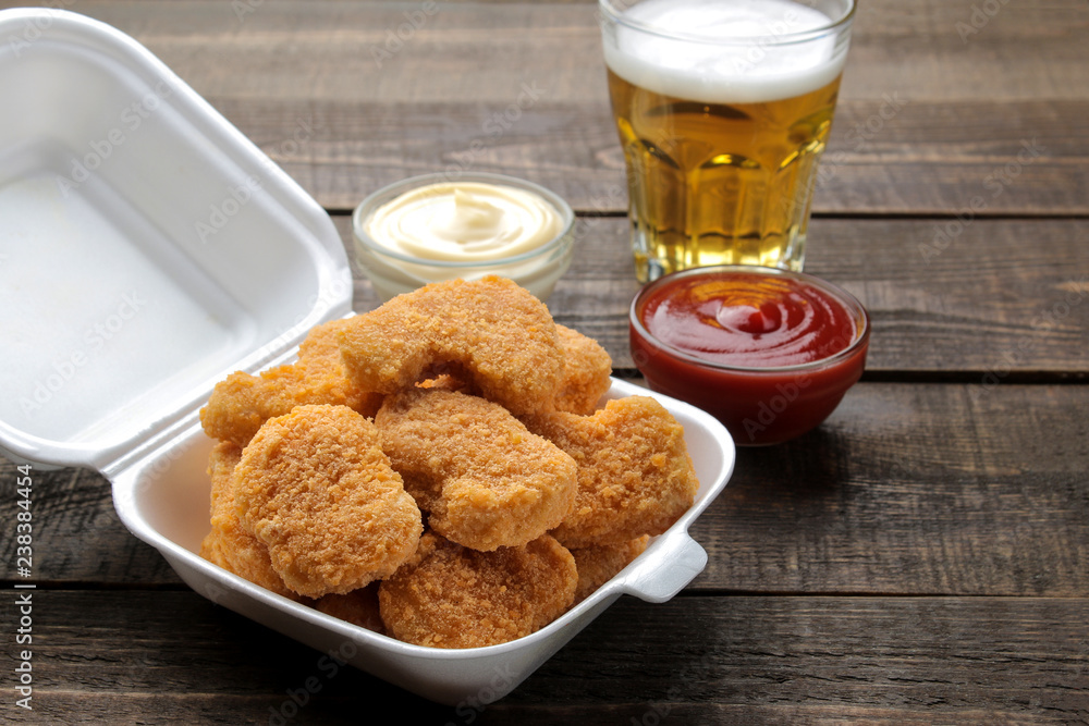 chicken nuggets in a food delivery box with white and red sauce and beer on a brown wooden background. fast food chicken nuggets in a food delivery box with white and red sauce and beer on a brown wooden background. fast food