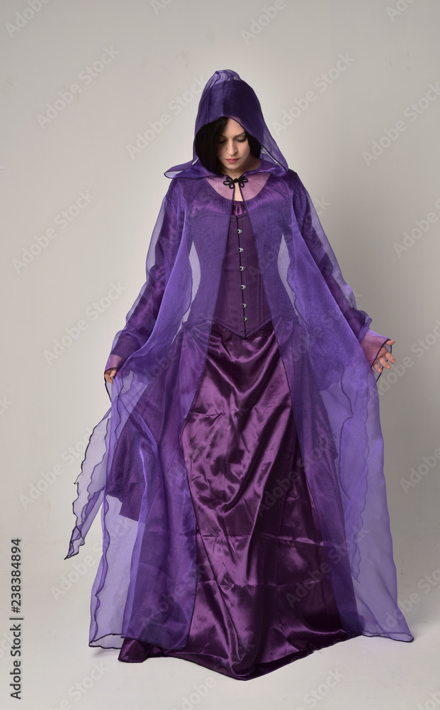 full length portrait of beautiful girl with long black hair, wearing purple fantasy medieval gown and cloak. standing pose on grey studio background. full length portrait of beautiful girl with long black hair, wearing purple fantasy medieval gown and cloak. standing pose on grey studio background.