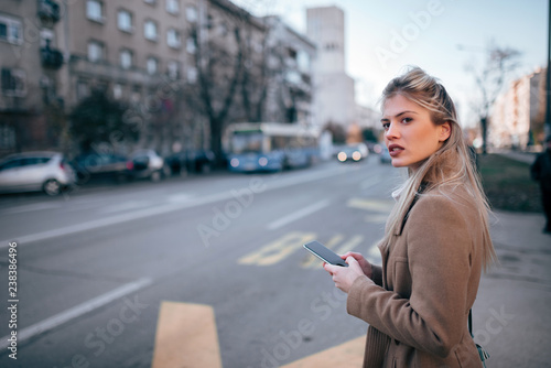 Beautiful young stylish woman using smartpone while waiting for taxi or bus in the city. © bnenin