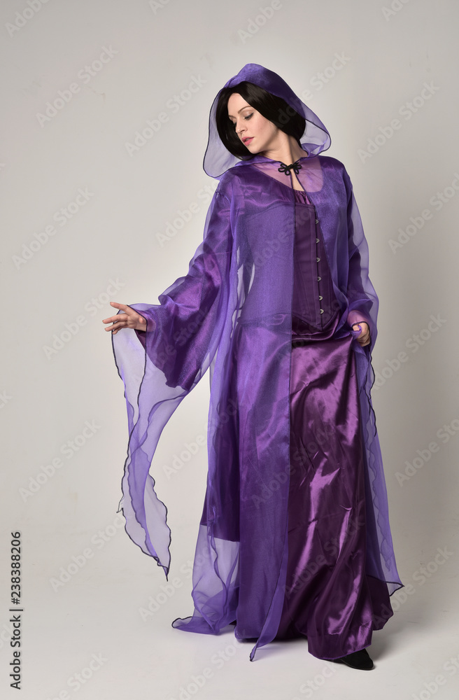 full length portrait of beautiful girl with long black hair, wearing purple fantasy medieval gown and cloak. standing pose on grey studio background. full length portrait of beautiful girl with long black hair, wearing purple fantasy medieval gown and cloak. standing pose on grey studio background.