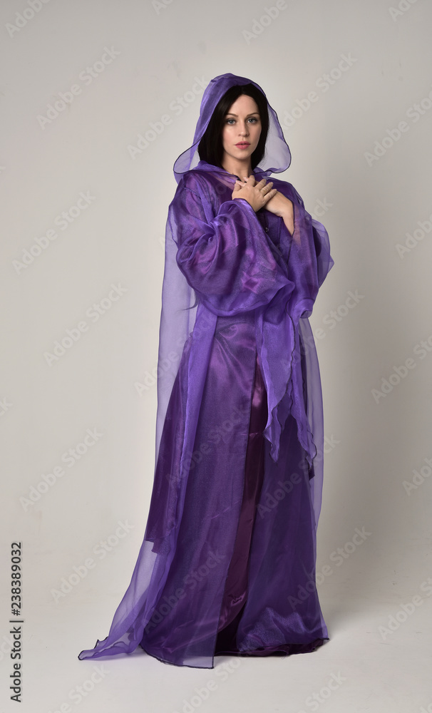 full length portrait of beautiful girl with long black hair, wearing purple fantasy medieval gown and cloak. standing pose on grey studio background. full length portrait of beautiful girl with long black hair, wearing purple fantasy medieval gown and cloak. standing pose on grey studio background.