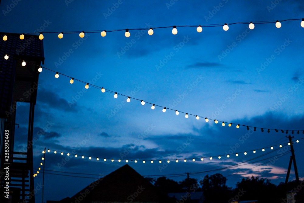 Row of hanging summer terrace lights during evening, small outdoor light bulbs.