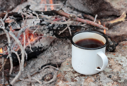 Tea in metal mug heats up on stone on bonfire.