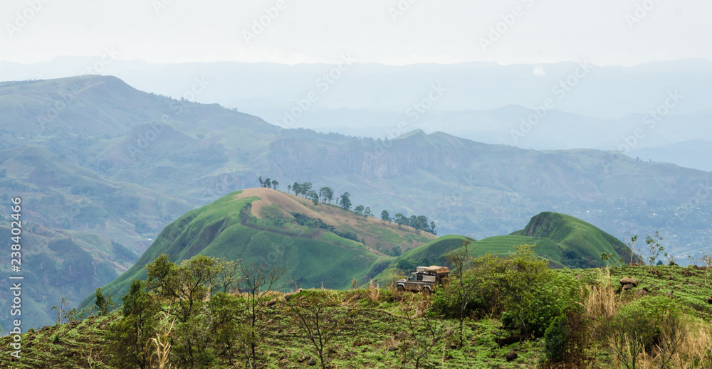 4x4 vehicle in rolling fertile hills with fields and crops on Ring Road of Cameroon, Africa.