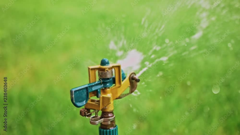 Sprinkler on tripod spreading water over the grass in slomo Sprinkler on tripod spreading water over the grass in slomo