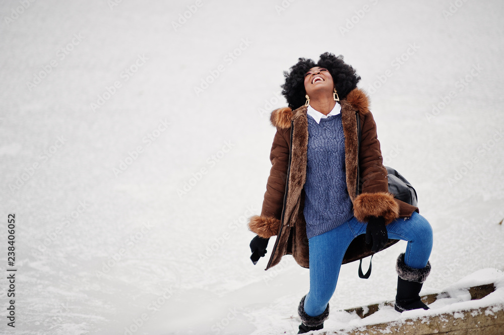 Curly hair african american woman wear on sheepskin coat and gloves with backpack posed at winter day.