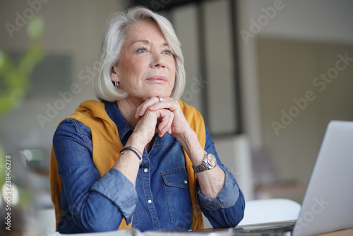 Fotografie, Obraz Beautiful senior woman looking pensive at home with laptop