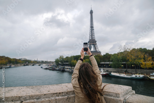 Young woman taking photo of Eiffel tower in Paris with smartphone, travel in Europe. Paris, France