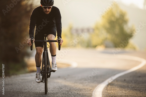 Professional road bicycle racer in action. Men cycling mountain road bike at sunset.
