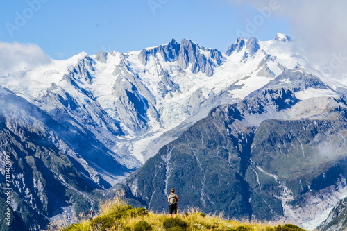 Travel New Zealand, Mount Fox. Scenic view of snowy southern alps, mount cook and glaciers. Small person / tourist woman with hands up enjoying life. Outdoor/travel freedom content.