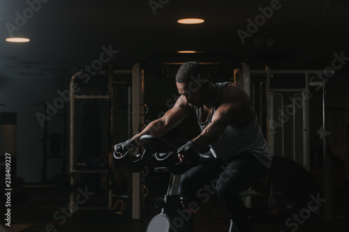 Serious black man on exercise bike in gym