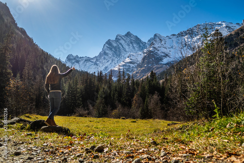 Beautiful young woman on meadow in meadle of coniferous forest in front of high snow covered mountain range photo