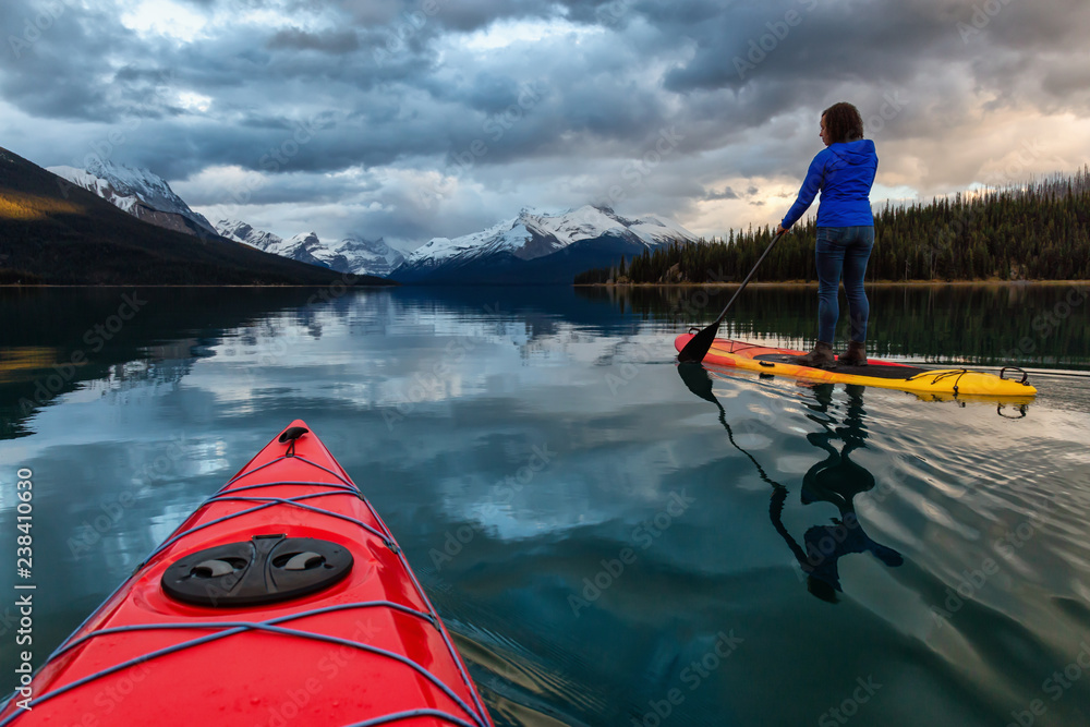 Kayaking in a peaceful and calm glacier lake during a vibrant cloudy sunset. Taken in Maligne Lake, Jasper National Park, Alberta, Canada. Kayaking in a peaceful and calm glacier lake during a vibrant cloudy sunset. Taken in Maligne Lake, Jasper National Park, Alberta, Canada.
