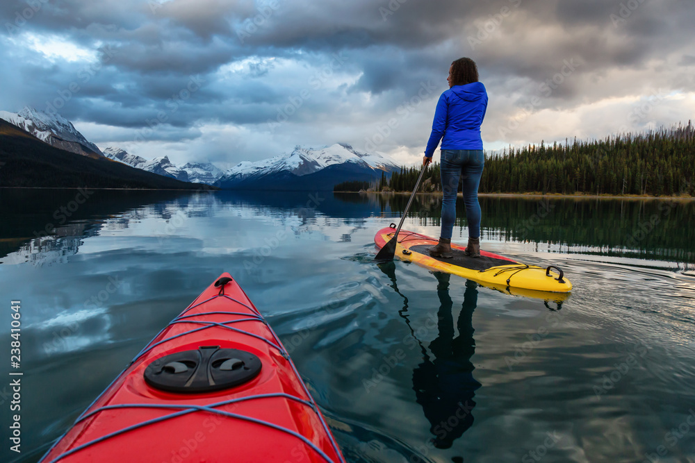 Kayaking in a peaceful and calm glacier lake during a vibrant cloudy sunset. Taken in Maligne Lake, Jasper National Park, Alberta, Canada. Kayaking in a peaceful and calm glacier lake during a vibrant cloudy sunset. Taken in Maligne Lake, Jasper National Park, Alberta, Canada.