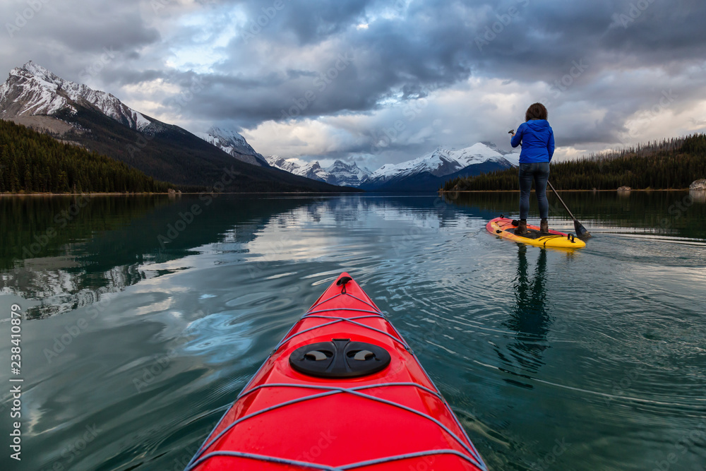 Kayaking in a peaceful and calm glacier lake during a vibrant cloudy sunset. Taken in Maligne Lake, Jasper National Park, Alberta, Canada. Kayaking in a peaceful and calm glacier lake during a vibrant cloudy sunset. Taken in Maligne Lake, Jasper National Park, Alberta, Canada.