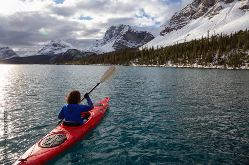 Adventurous girl kayaking in a glacier lake surrounded by the Canadian Rockies during a cloudy morning. Taken at Bow Lake  Banff  Alberta  Canada.