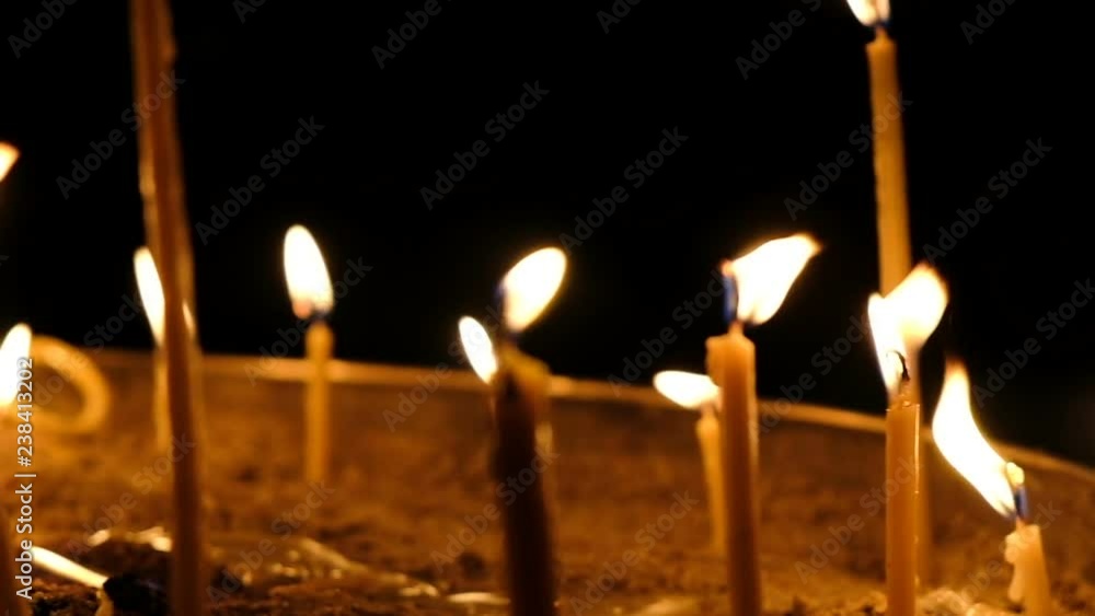 Wax candles burn in the dark in church against dark background close-up camera movement, slow motion Wax candles burn in the dark in church against dark background close-up camera movement, slow motion