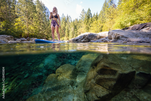 Over and Under Picture of a young Caucasian girl paddle boarding in a river during a sunny summer day. Taken in Alouette Lake, near Vancouver, BC, Canada.