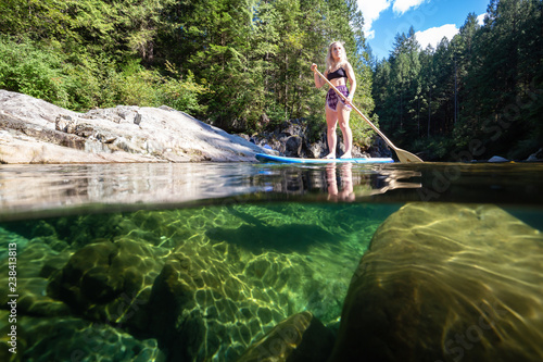 Over and Under Picture of a young Caucasian girl paddle boarding in a river during a sunny summer day. Taken in Alouette Lake, near Vancouver, BC, Canada. photo