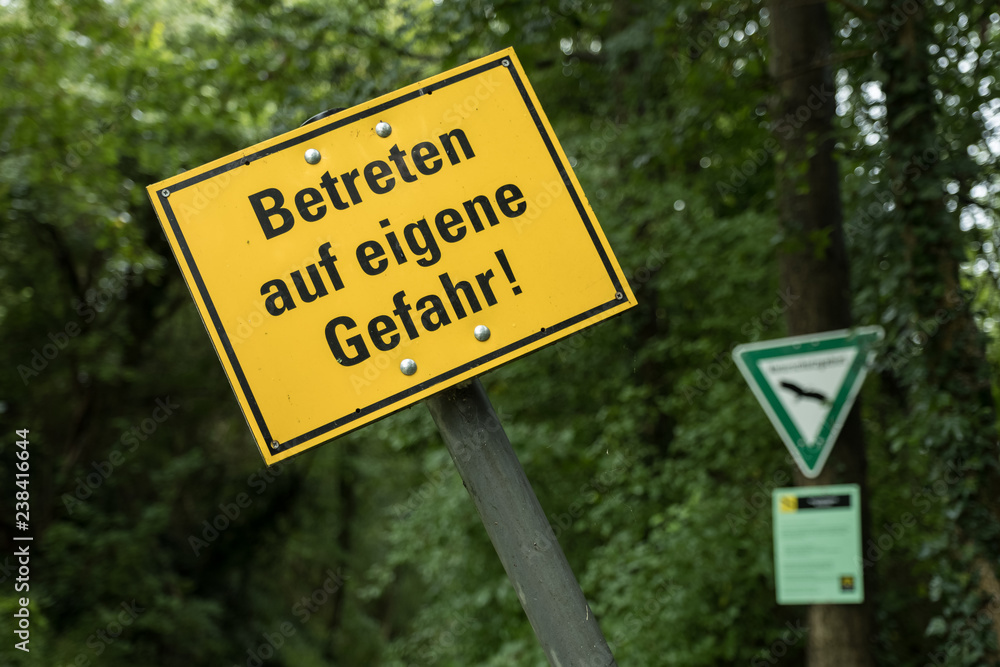 Gelbes Warnschild Betreten auf eigene Gefahr vor unscharfem Wald