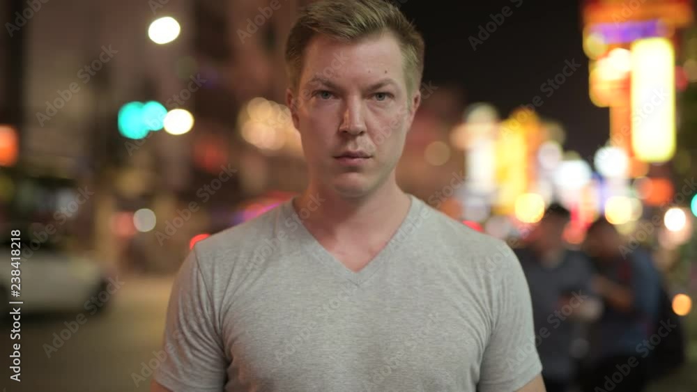 Young happy tourist man smiling against view of the streets in Chinatown at night Young happy tourist man smiling against view of the streets in Chinatown at night