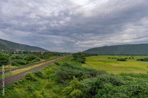 straight railway track goes to horizon in green landscape under blue sky with clouds. © Mayank