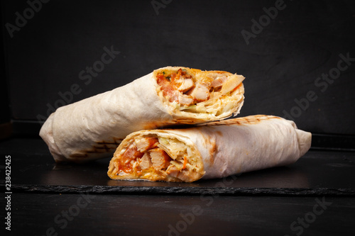 Shawarma sandwich gyro- fresh roll of thin lavash (pita bread) filled with grilled meat, mushrooms, cheese, cabbage, carrots, sauce, green. Traditional Eastern snack. On dark black background photo