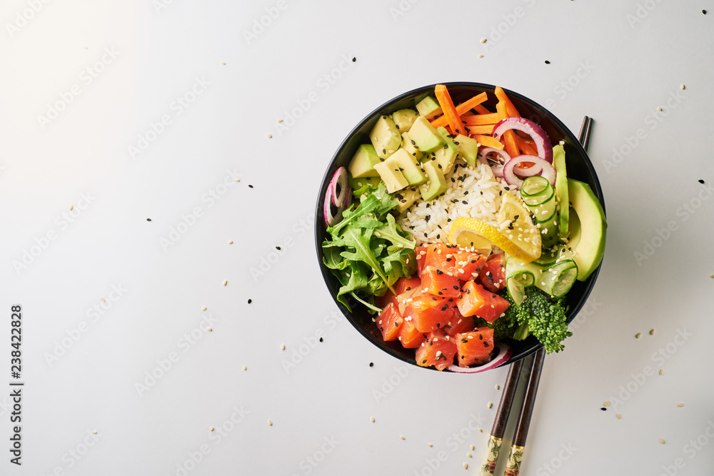 poke bowl with salmon, avocado, cucumber, arugula, broccoli, rice, carrot and sweet onions with chopsticks isolated over white background. top view