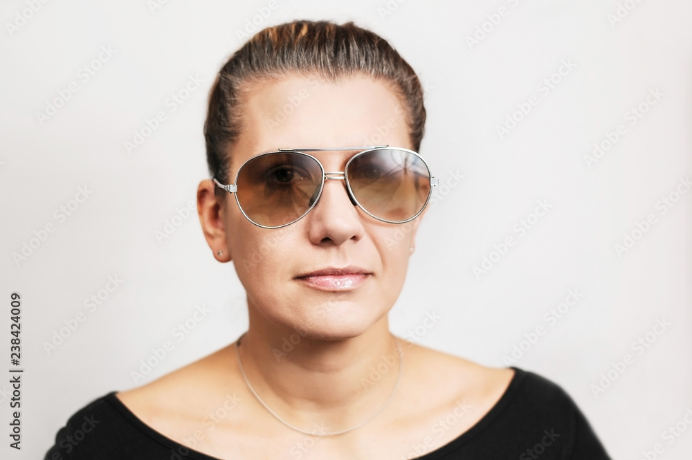 A good middle-aged woman in glasses from the sun on a light background. Hair in a woman begins to become gray A good middle-aged woman in glasses from the sun on a light background. Hair in a woman begins to become gray