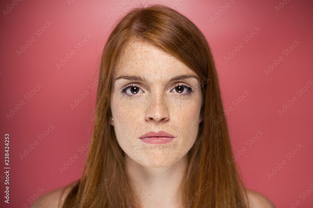 Redhead young serious woman looking at camera over pink background. Redhead young serious woman looking at camera over pink background.
