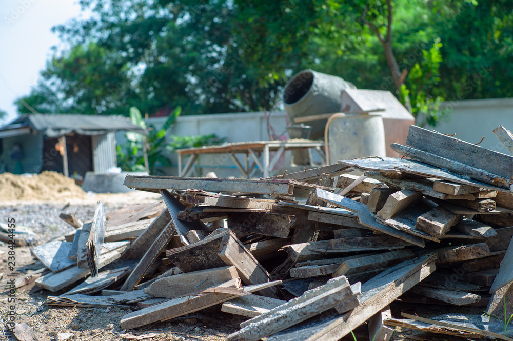 Closeup pile of useless wood at the construction site with blurred concrete mixer in background Closeup pile of useless wood at the construction site with blurred concrete mixer in background