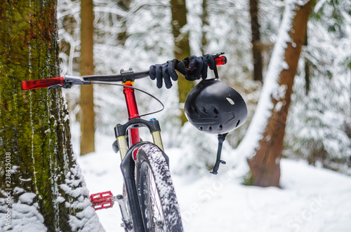 Black helmet with black sport gloves hangs on the handlebars of a bicycle in snowy winter forest. Mountain bike safety concept. Extreme sport background