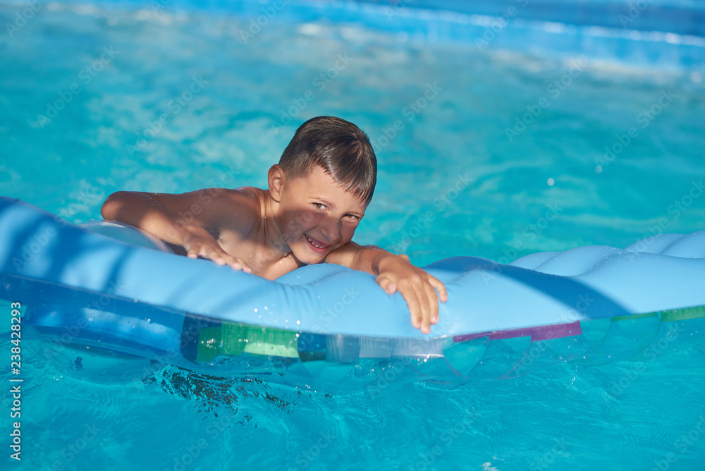 Portrait of happy Caucasian boy having fun with inflatable mattress in swimming pool at resort.