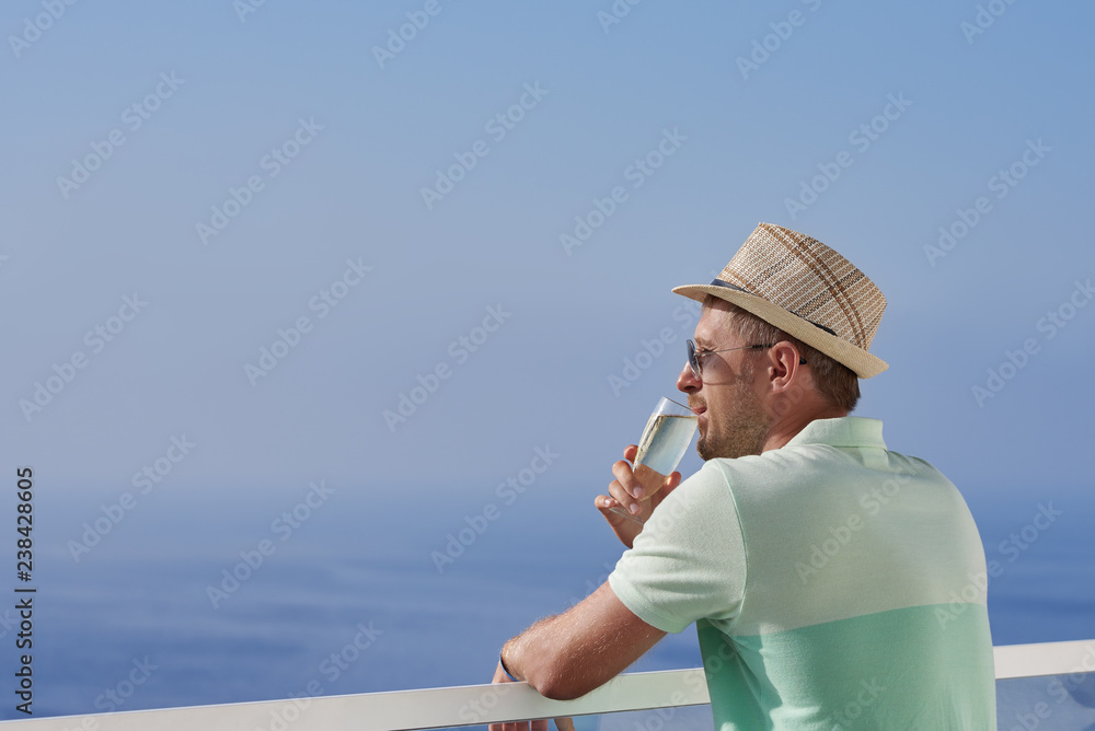 Man in sun hat and sunglasses drinking sparkling wine and enjoying beautiful blue sea view.