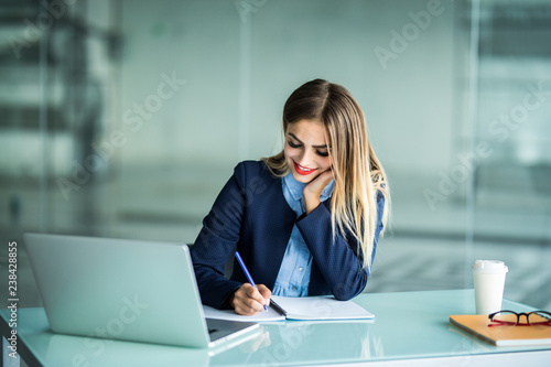 Young woman working with laptop and taking notes on a desktop at Office