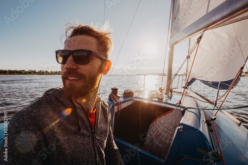 Captain of the yacht wearing sunglasses in a race on a river or sea at sunset