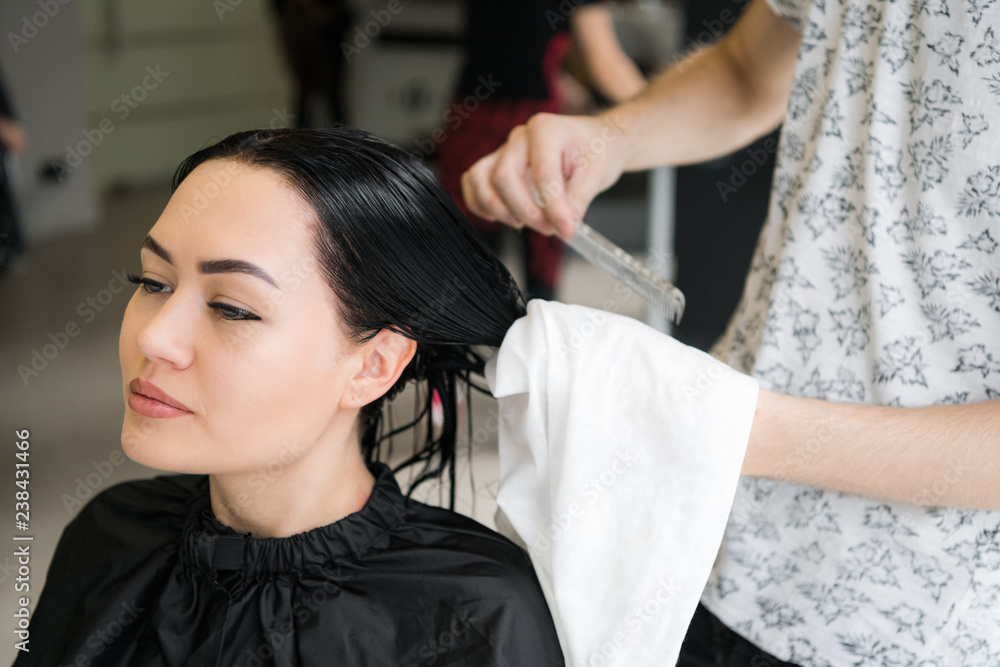 Fototapeta premium Hairdresser wrapping towel on customer's head. Brunette woman getting hair treatment in a salon.
