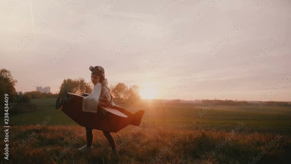 Happy little boy in fun cardboard plane costume spinning and landing on sunset autumn field playing pilot slow motion. Happy little boy in fun cardboard plane costume spinning and landing on sunset autumn field playing pilot slow motion.