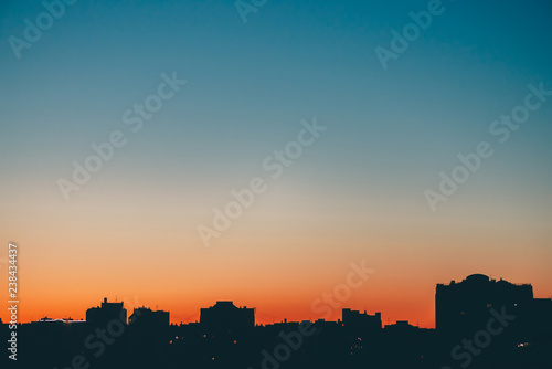 Cityscape with wonderful varicolored vivid dawn. Amazing blue sky with orange sunny light above dark silhouettes of city buildings. Atmospheric background of warm sunrise. Copy space.