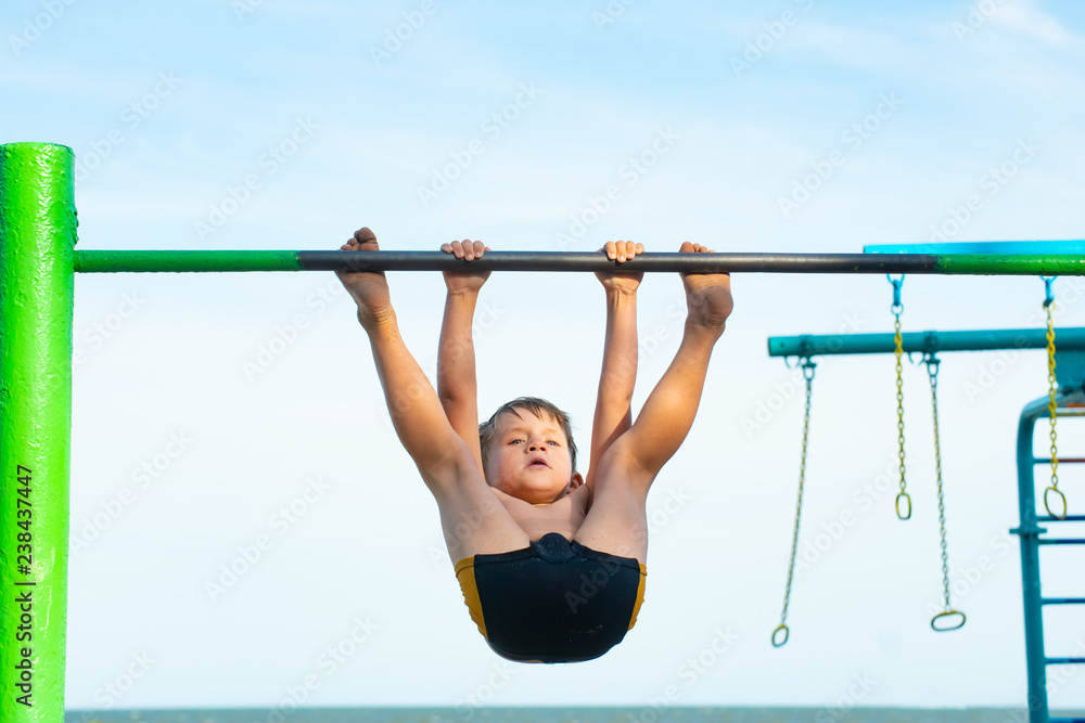 A little boy plays sports on a horizontal bar on the street, performs a workout in athletics. A little boy plays sports on a horizontal bar on the street, performs a workout in athletics.