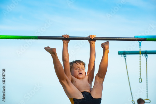 The boy in black shorts hangs on the bar and legs raised up.