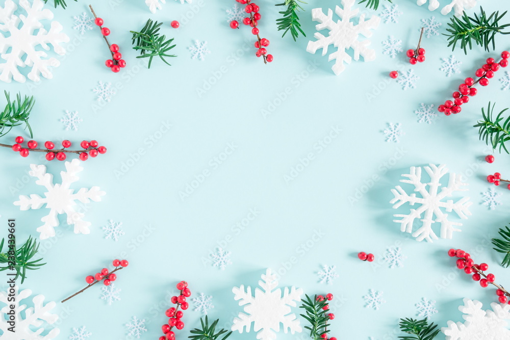 Christmas modern composition. Frame made of green fir tree branches, red berries and snowflakes on pastel blue background. Christmas, New Year, winter concept. Flat lay, top view, copy space Christmas modern composition. Frame made of green fir tree branches, red berries and snowflakes on pastel blue background. Christmas, New Year, winter concept. Flat lay, top view, copy space