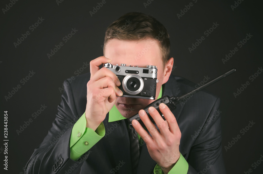 Φωτογραφία Spy secret service agent with photo camera is photographing a compromising evidence and is talking on a portable radio station isolated on the black background