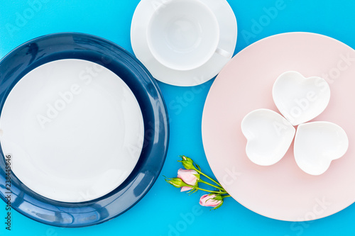 Simple color table setting for celebration with roses, blue and pink plates and heart-shaped saucers on blue table background top view mock up
