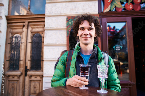 Image of smiling man tourist standing outdoors in city street cafe holding glass drinking wine. Tourist in the old Lviv, Ukraine.